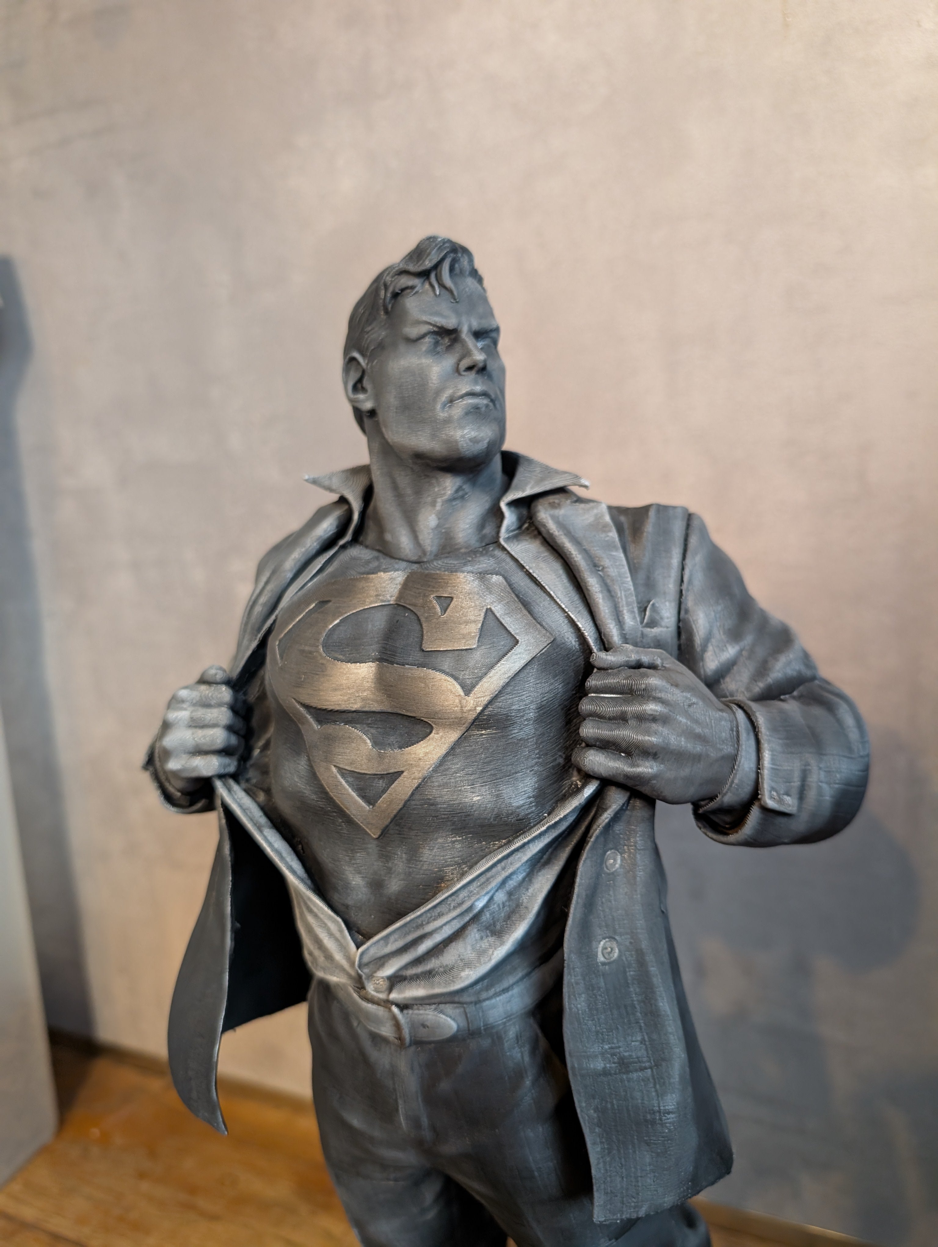 Statue of a superhero with a chest emblem, resembling Superman, against a neutral background.