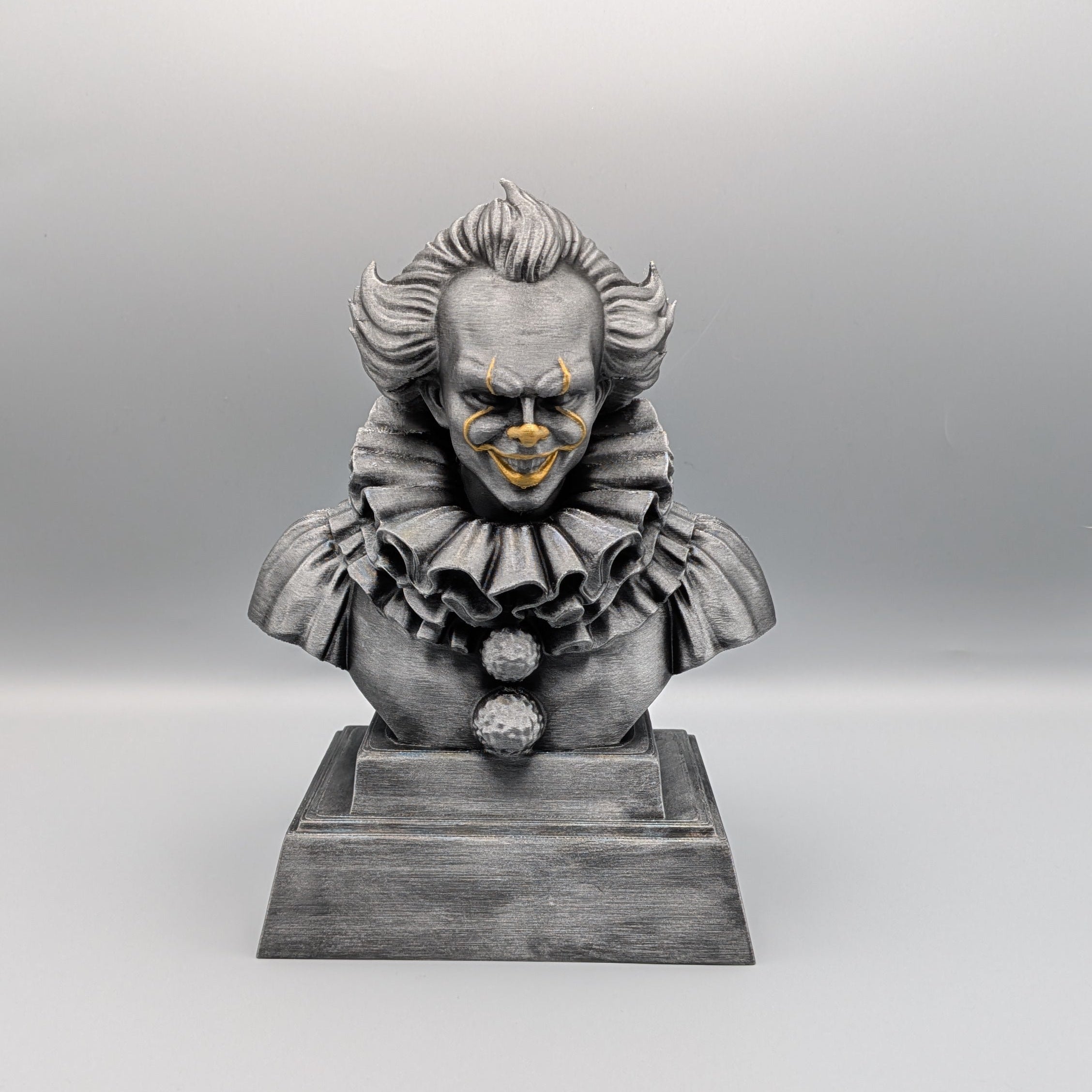 Front view of a 20 cm hand-painted silver Pennywise tribute bust with gold facial accents on a pedestal base