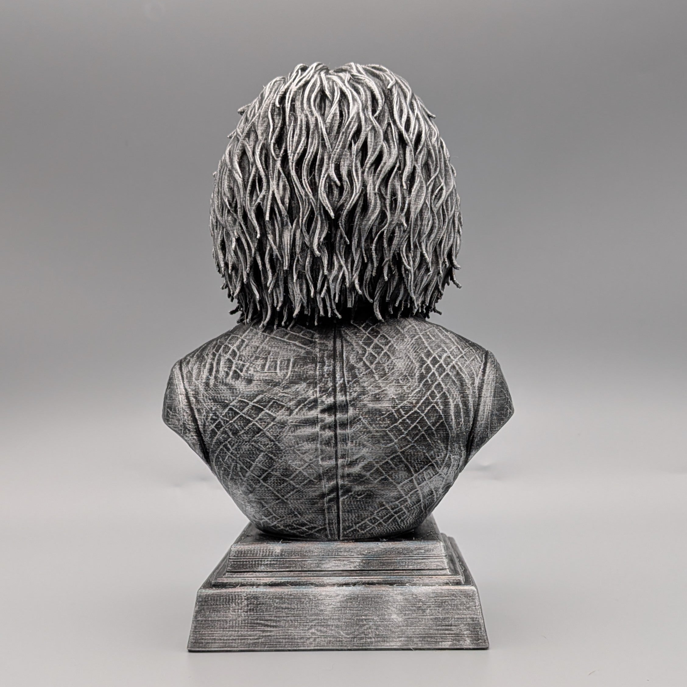 Rear view of a silver Saw-inspired horror puppet bust, showing sculpted hair, textured suit and pedestal base.
