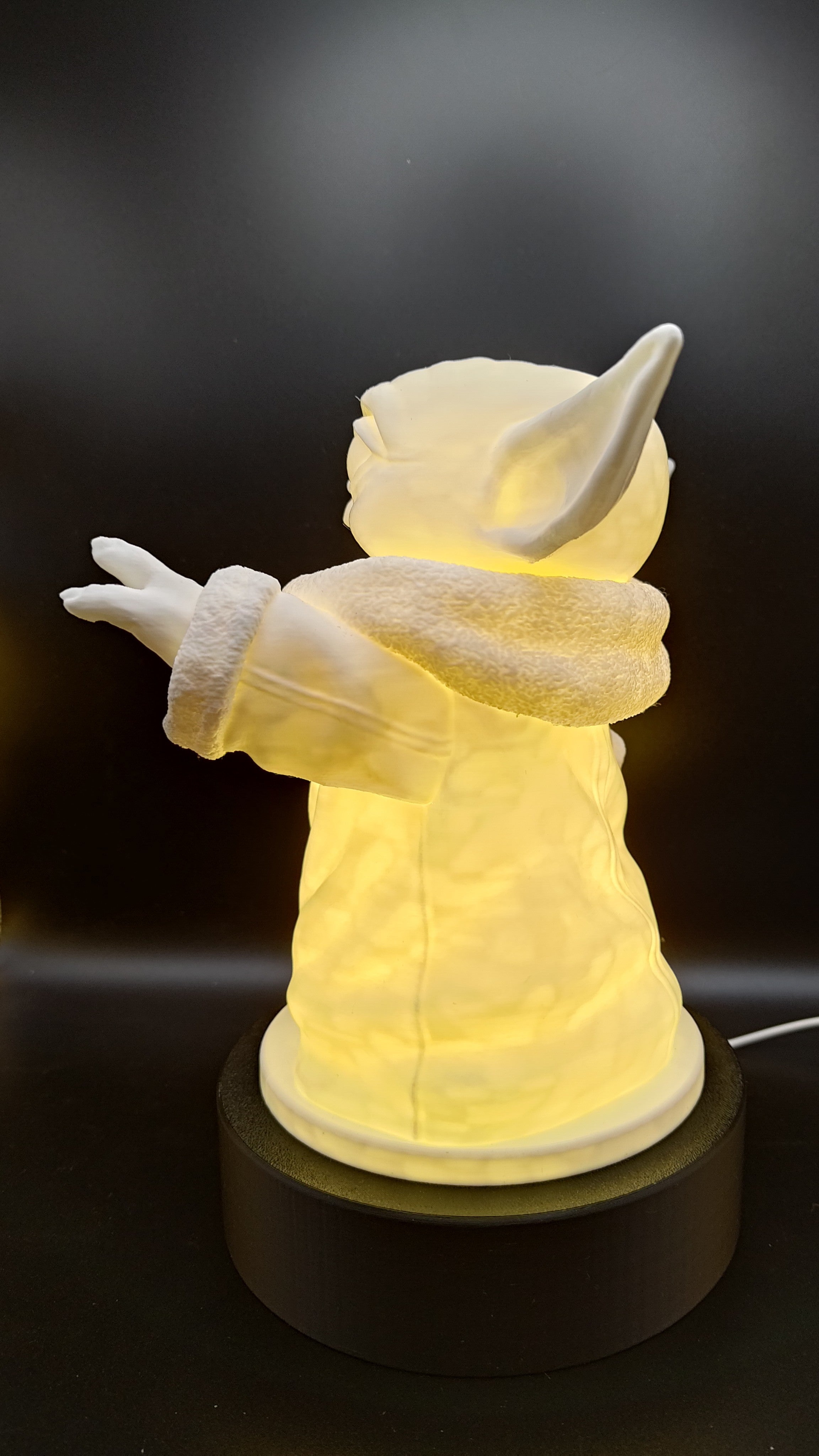 Side view of the illuminated Grogu lamp showing the raised hand and detailed robe