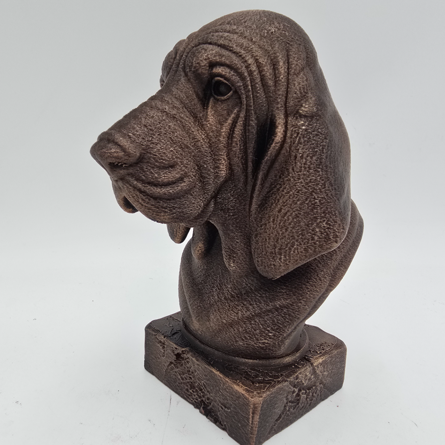 Bronze Bloodhound dog bust sculpture viewed from the front left, featuring long drooping ears and detailed facial folds.