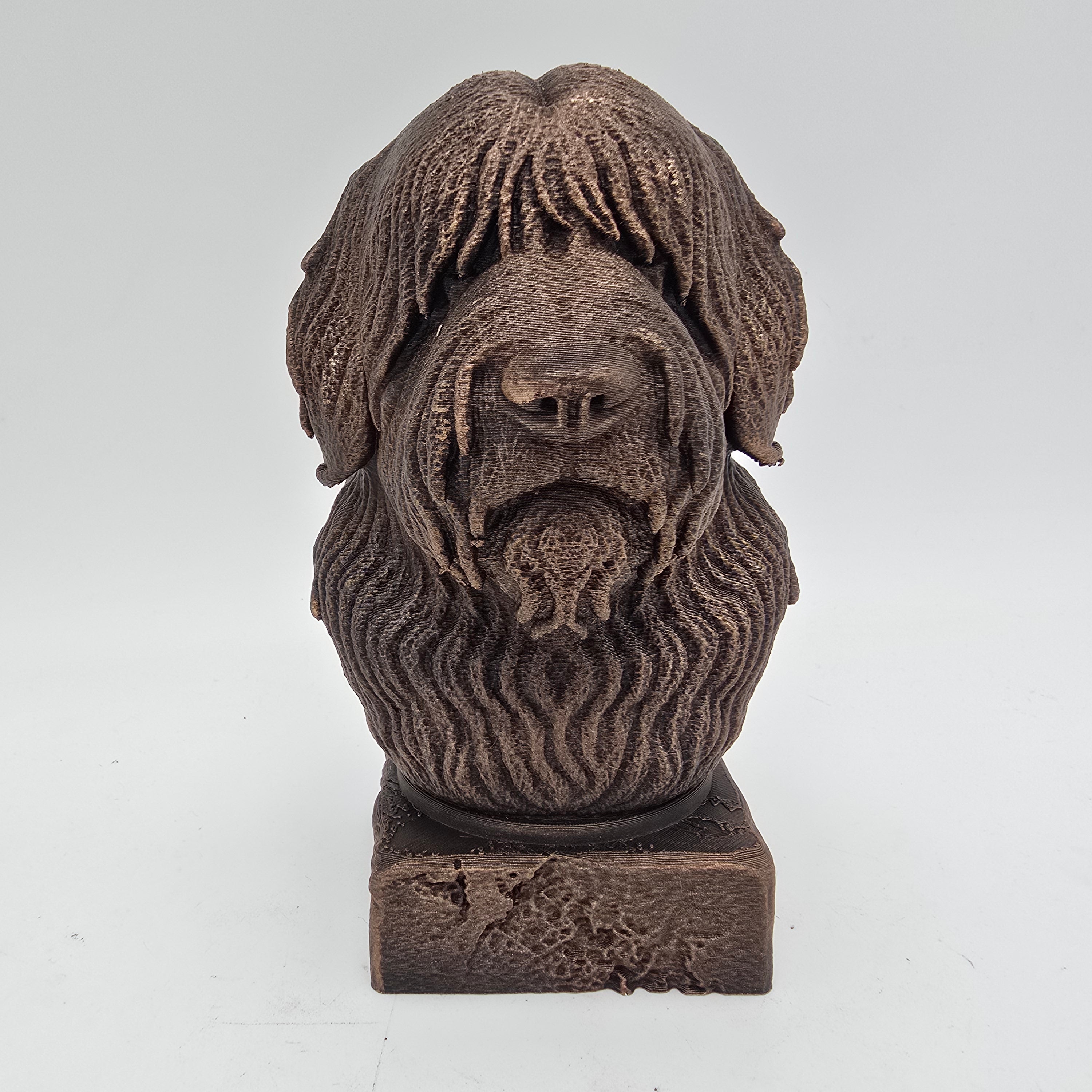 Front view of a bronze Bobtail dog bust sculpture with detailed shaggy fur on a decorative pedestal.