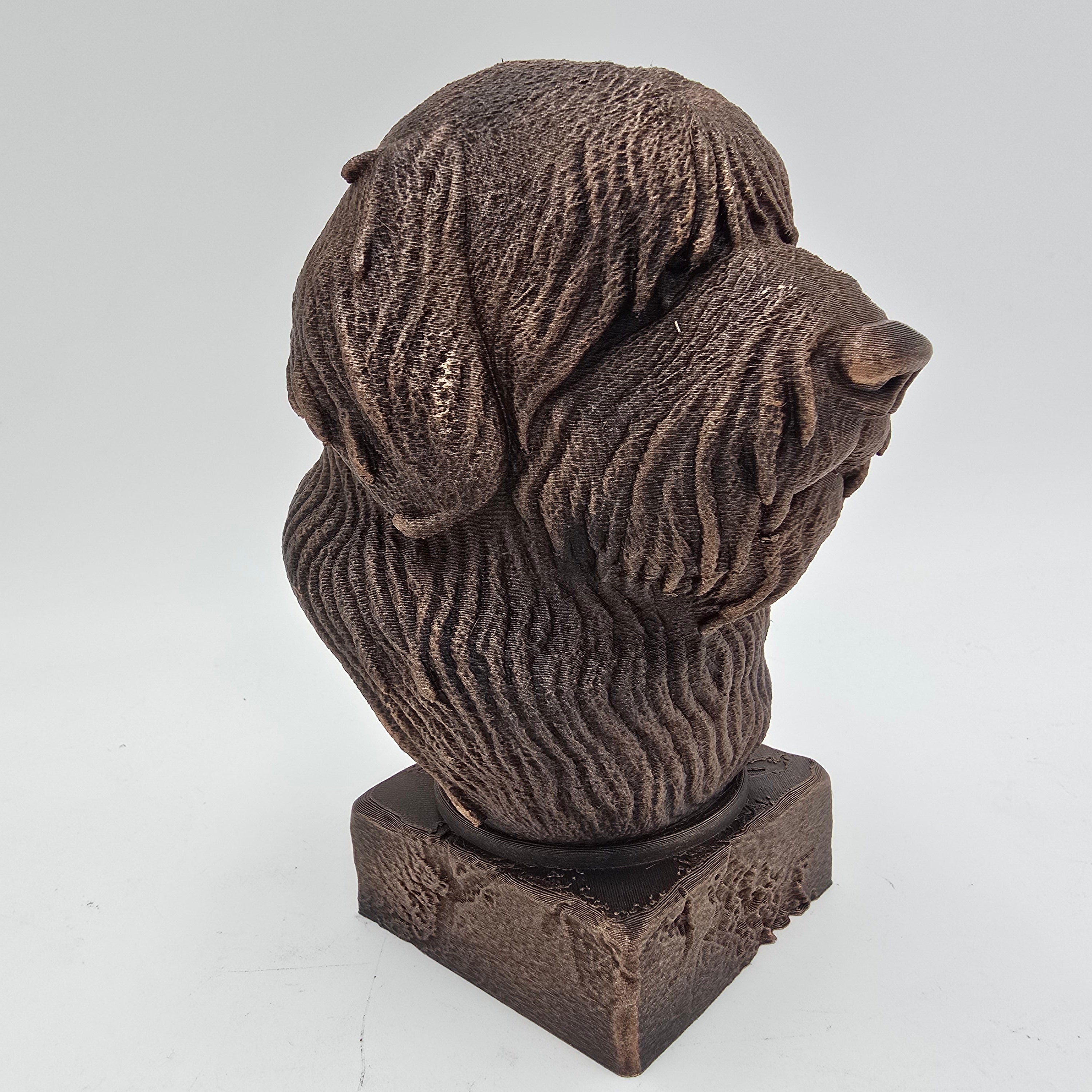 Bronze Bobtail dog bust sculpture viewed from the front right, featuring long shaggy fur and a decorative pedestal.