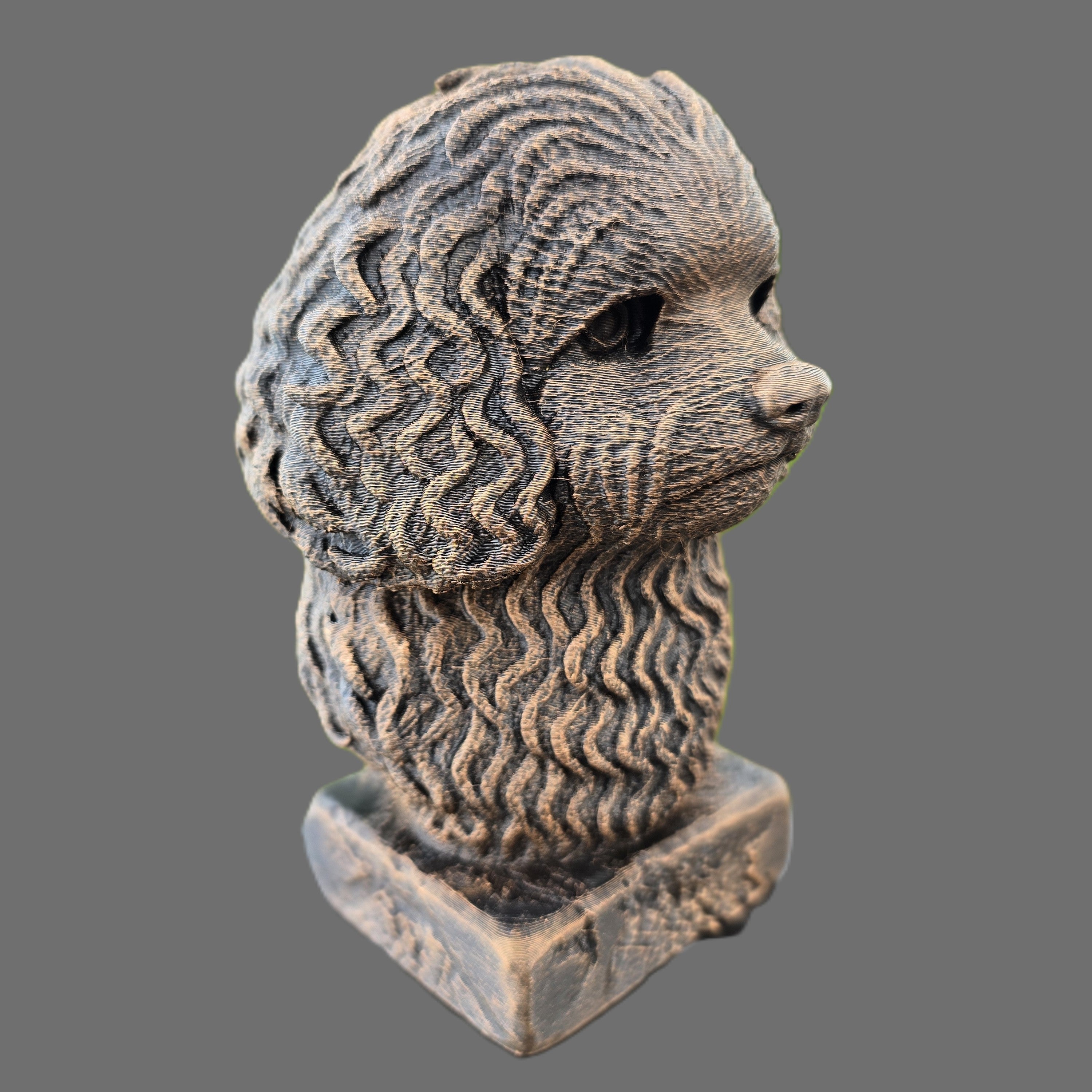 A textured decorative sculpture of a balonka dog's head in profile, mounted on a square base, shown against a solid gray background.