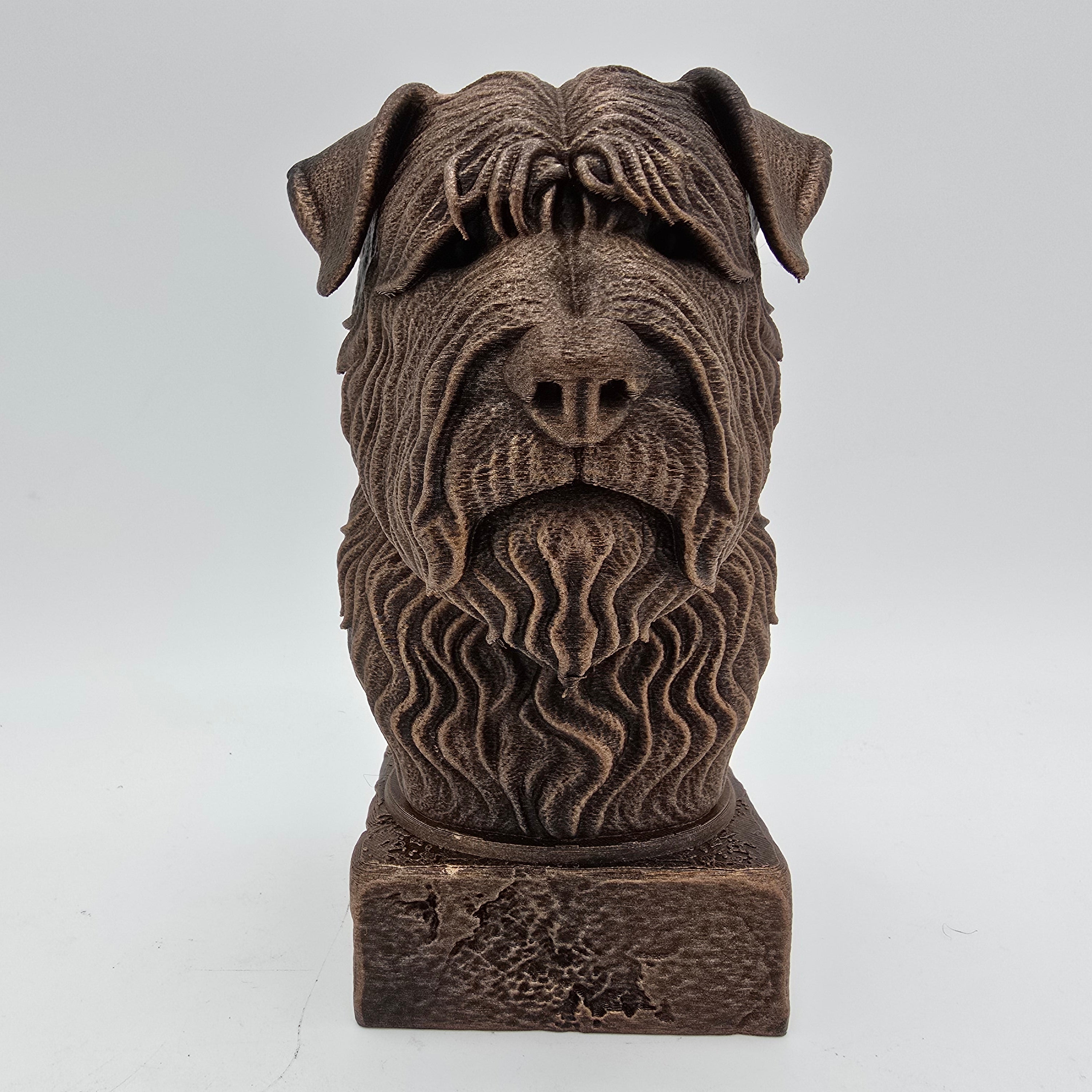 Front view of a bronze Bouvier des Flandres dog bust sculpture with shaggy fur and a distinctive beard on a decorative pedestal.