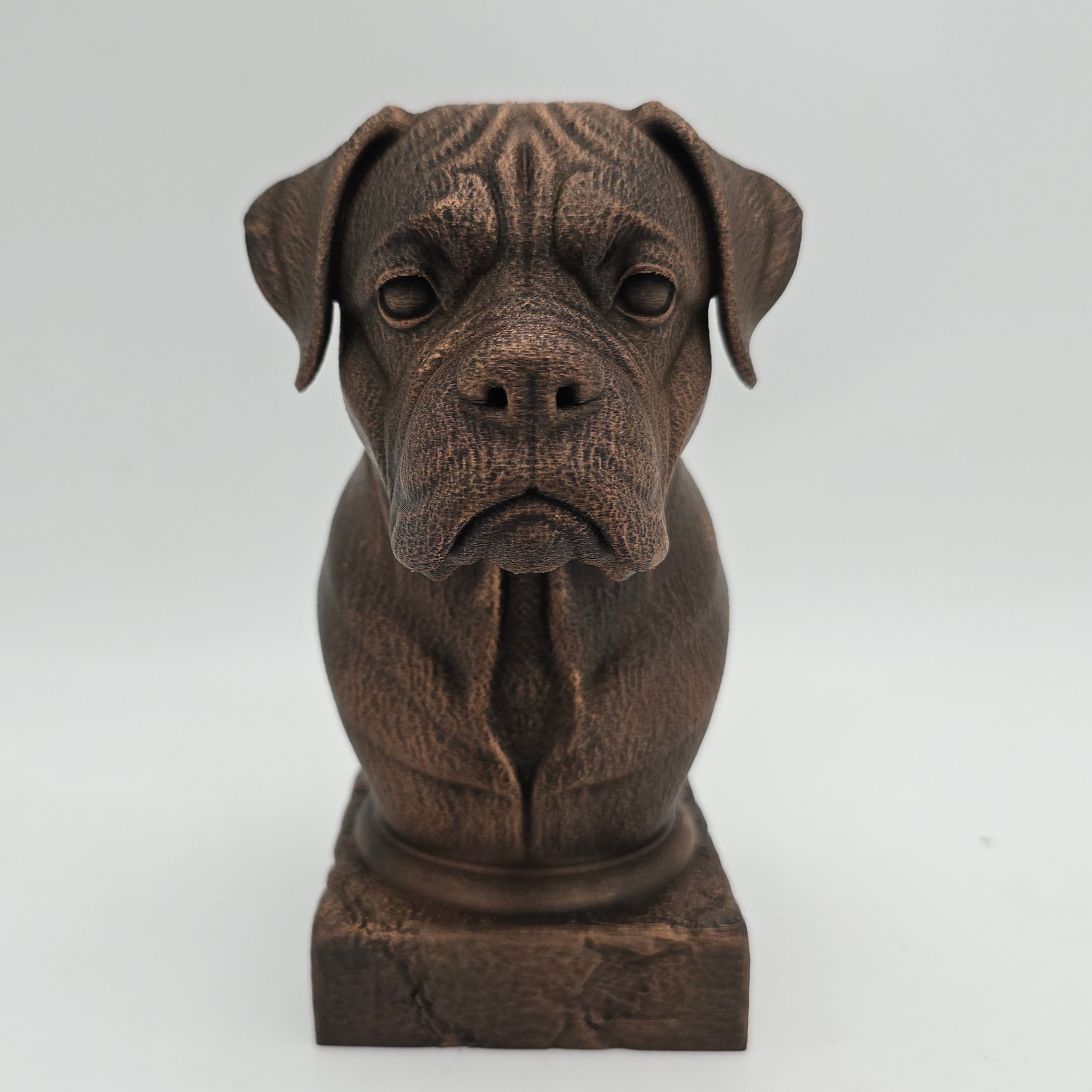 Front view of a bronze Boxer dog bust sculpture with folded ears, a broad muzzle and detailed facial features on a decorative pedestal.