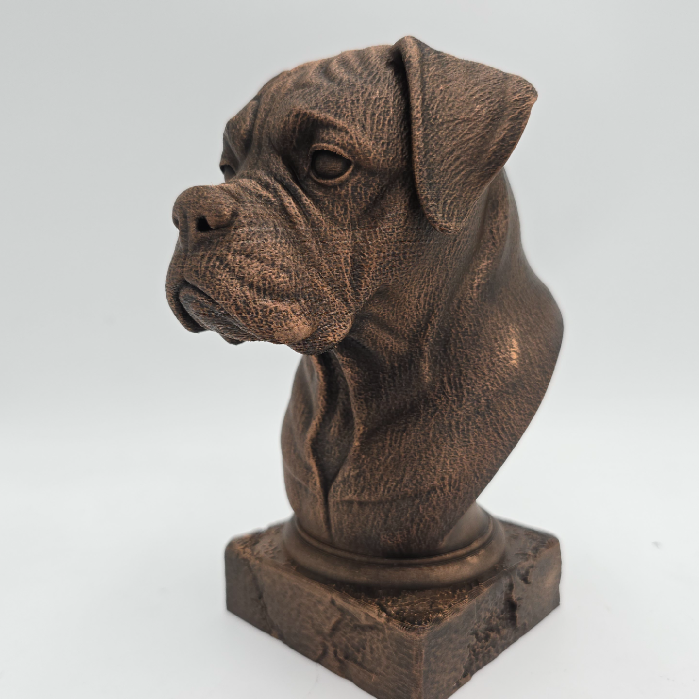 Bronze Boxer dog bust sculpture viewed from the front left, featuring folded ears, a broad muzzle and detailed facial features on a decorative pedestal.