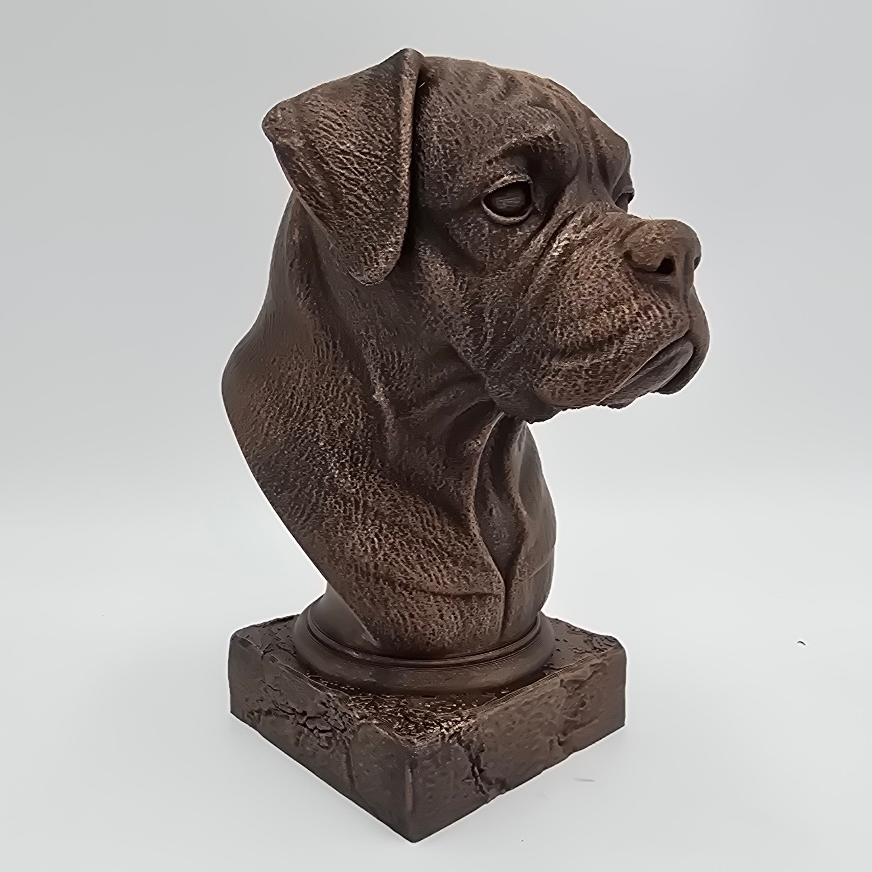 Bronze Boxer dog bust sculpture viewed from the front right, featuring folded ears, a broad muzzle and detailed facial features on a decorative pedestal.