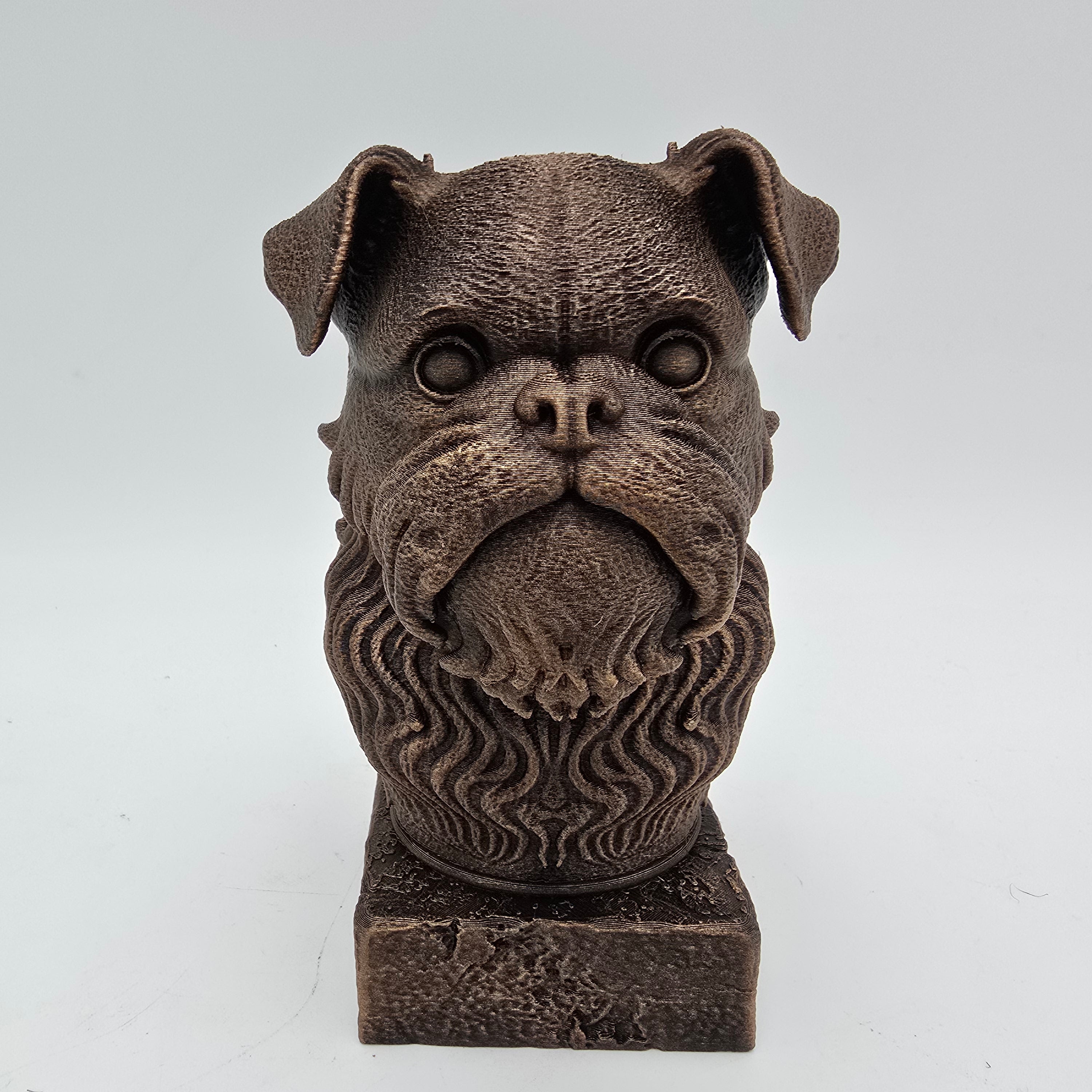 Front view of a bronze Brussels Griffon dog bust sculpture with large eyes, a short muzzle and detailed beard on a decorative pedestal.